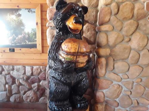 A wooden bear statue holding a large hamburger, set against a stone wall.