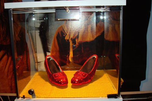 A pair of sparkling red shoes displayed in a glass case on a yellow surface.