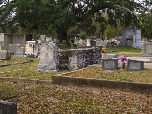 A peaceful cemetery scene with various gravestones, surrounded by trees and scattered flowers.