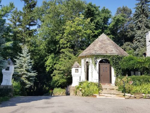 A charming stone building with a conical roof, surrounded by lush greenery and trees.
