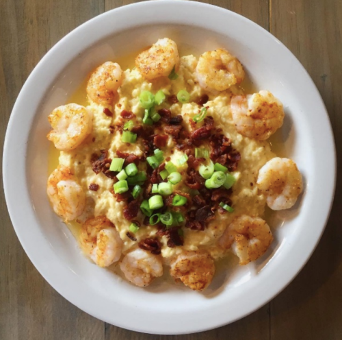 A bowl of creamy grits topped with shrimp, crispy bacon, and green onions.
