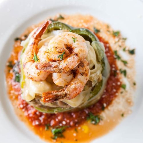 A plate of shrimp atop fettuccine, garnished with herbs and served with a rich tomato sauce.