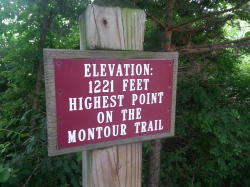 Sign indicating the highest point on the Montour Trail, with an elevation of 1221 feet, surrounded by greenery.