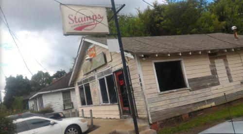 A weathered building with a sign for "Stamps Super Burgers," surrounded by trees and parked cars.