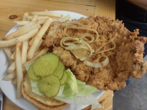 A plate of fried chicken with onions, pickles, lettuce, and fries, served on a wooden table.