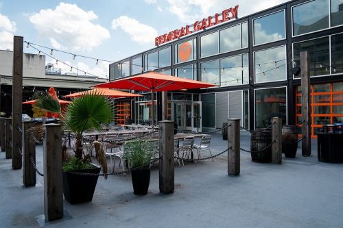 Outdoor seating area of Federal Galley with orange umbrellas, planters, and modern glass architecture.