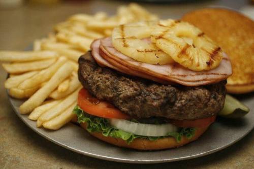 A juicy burger topped with ham and grilled pineapple, served with fries on a plate.