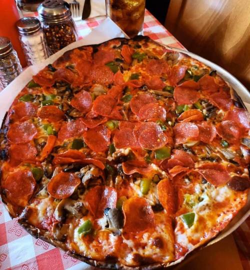 A large pizza topped with pepperoni, green peppers, mushrooms, and cheese on a checkered tablecloth.
