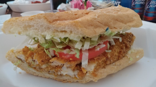 A close-up of a crispy chicken sandwich with lettuce and tomato on a toasted bun, served on a white plate.