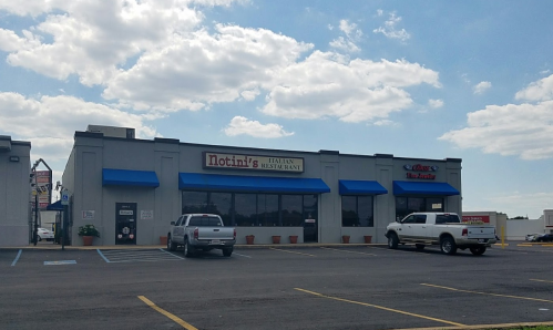 Exterior of Nottini's Italian Restaurant with blue awnings and parked white trucks under a partly cloudy sky.