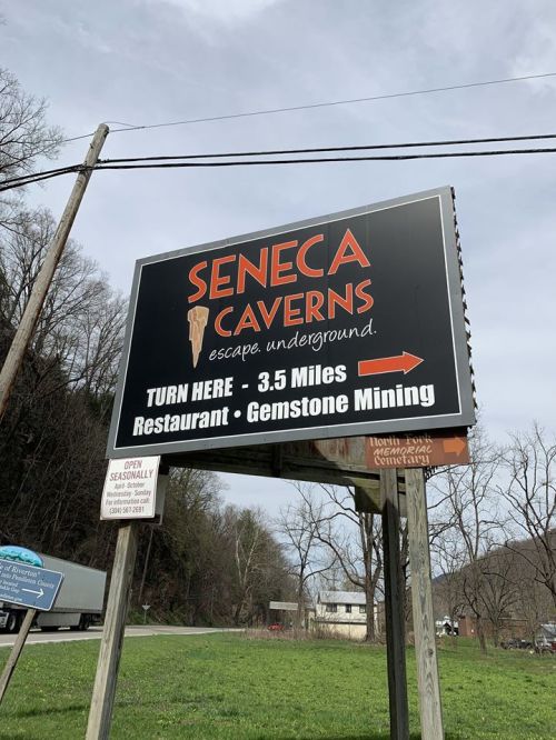 Sign for Seneca Caverns, indicating directions, distance, and activities like gemstone mining and dining.