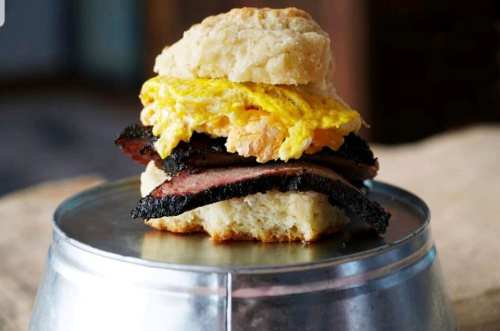 A biscuit sandwich with layers of brisket and fluffy scrambled eggs, served on a metal surface.