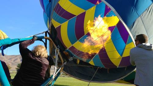 A hot air balloon being inflated, with flames shooting from the burner as two people assist in the process.