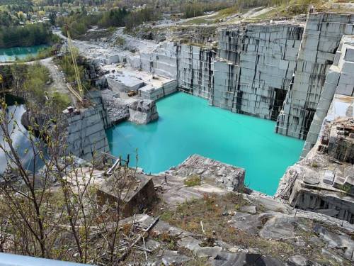 A turquoise water-filled quarry surrounded by steep stone walls and greenery in the background.