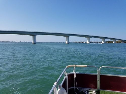 A view of a bridge spanning over calm blue waters, seen from a boat. Clear skies above.