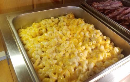 A metal tray filled with creamy macaroni and cheese topped with melted cheddar cheese.