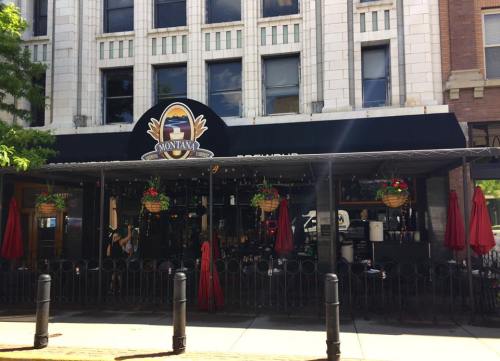 Exterior of Montana restaurant with a black awning, red umbrellas, and hanging flower baskets on a sunny day.