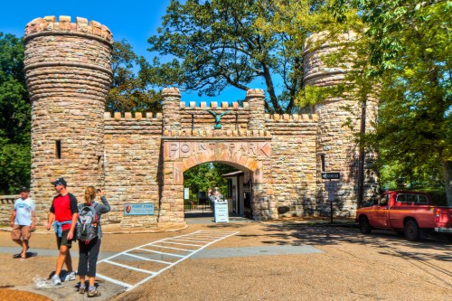 Stone entrance to Point Park with two towers, surrounded by trees and visitors walking by. A red truck is parked nearby.