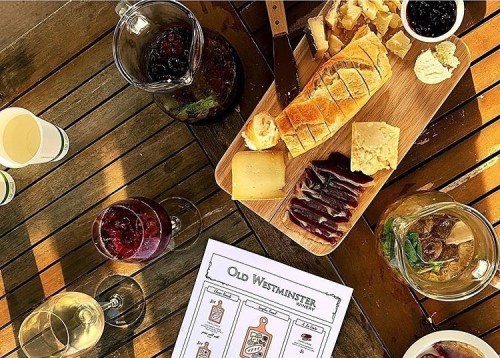 A wooden table with a charcuterie board, wine glasses, and a menu, featuring cheese, bread, and preserves.