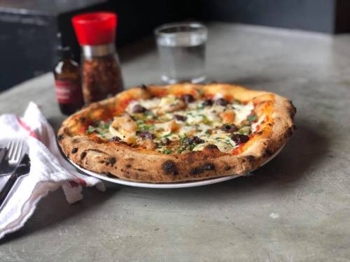 A freshly baked pizza with toppings on a white plate, accompanied by a glass of water and condiments on a table.