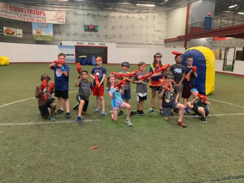 A group of children holding toy blasters, posing together in an indoor sports facility.