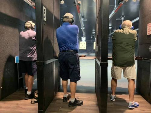 Three men at a shooting range, wearing ear protection and aiming at targets downrange.