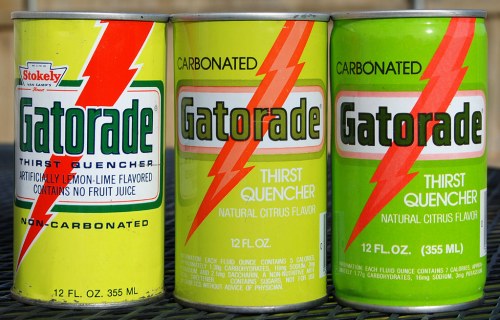 Three vintage Gatorade cans in yellow and green, labeled "Thirst Quencher" and "Carbonated," with lightning bolt designs.
