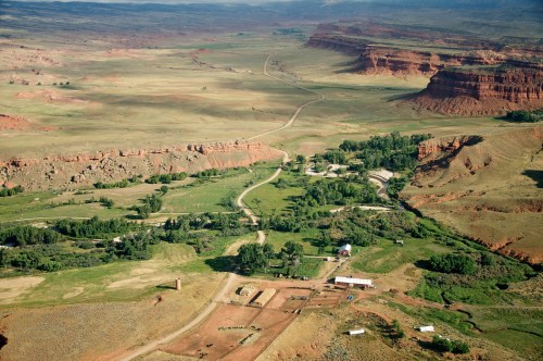 Aerial view of a vast, arid landscape with winding roads, green patches, and rocky formations in the distance.