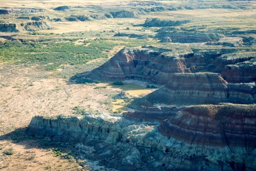 Aerial view of rugged, colorful rock formations and a sparse landscape with patches of greenery.