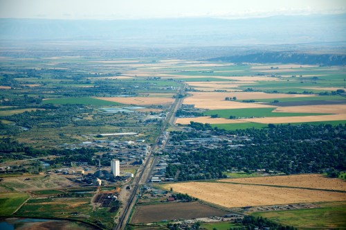 Aerial view of a rural landscape with fields, a small town, and a distant mountain range under a clear blue sky.