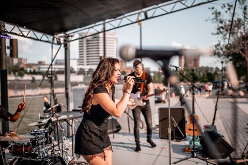 A singer performs on stage with a band, surrounded by instruments and a city skyline in the background.