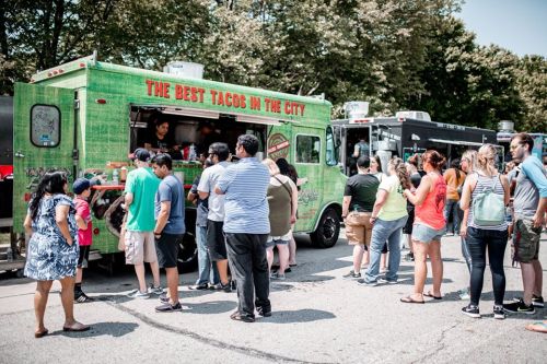 A busy food truck serving tacos, with a long line of people waiting to order on a sunny day.