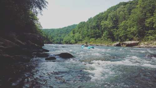 A person kayaking on a river surrounded by lush green hills and trees under a clear blue sky.