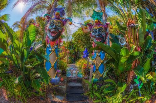 Colorful jester sculptures welcome visitors to a vibrant, lush garden path surrounded by tropical plants.