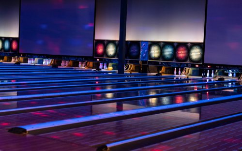 A vibrant bowling alley with illuminated lanes, colorful lights, and bowling pins set up at the end of the lanes.