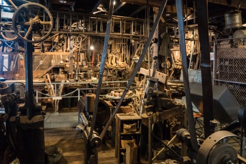 A cluttered workshop filled with various vintage machinery and tools, showcasing industrial equipment and wooden structures.