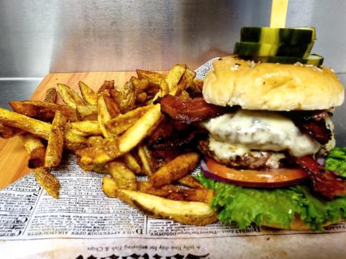 A juicy burger with bacon, cheese, lettuce, tomato, and pickles, served with a side of crispy fries on a wooden board.