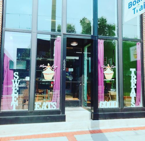 Storefront with large windows displaying "Sweet Eats" and "Good Treats" signs, featuring a cupcake graphic.