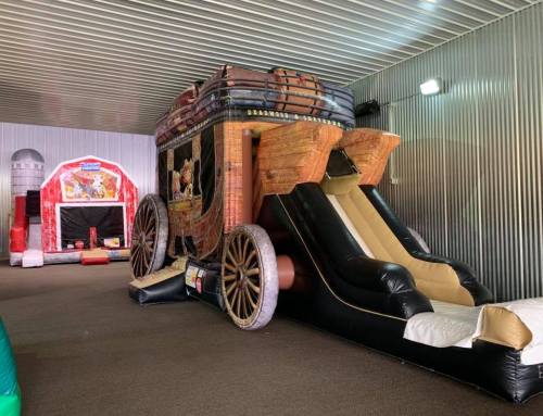 An inflatable slide designed like a western carriage, set in a spacious indoor play area with colorful decorations.