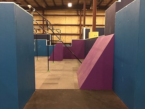 Indoor parkour gym featuring colorful walls and obstacles in blue and purple, with a spacious layout.