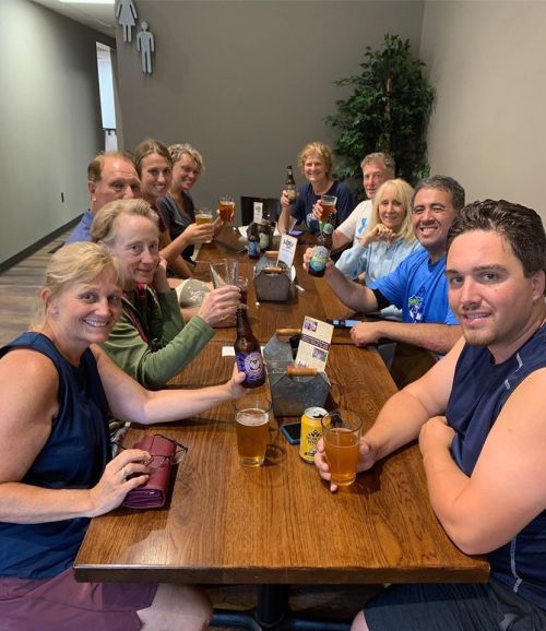 A group of twelve people sitting at a table, smiling and holding drinks in a casual setting.