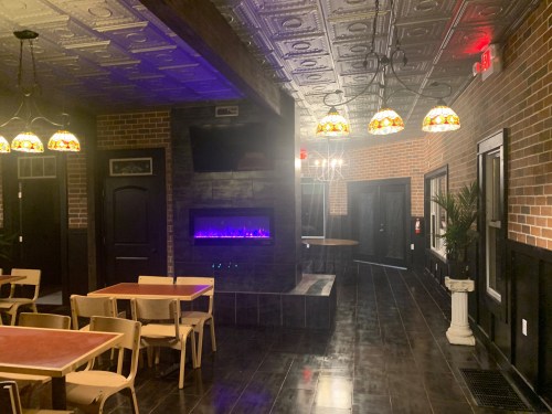 Interior of a restaurant featuring brick walls, a modern fireplace, and decorative lighting. Tables and chairs are arranged neatly.