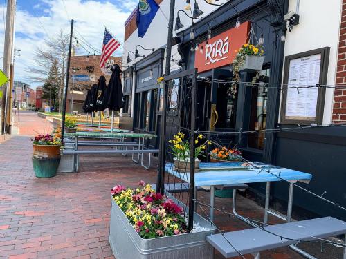 Outdoor seating area of a restaurant with colorful flowers, tables, and an American flag in the background.