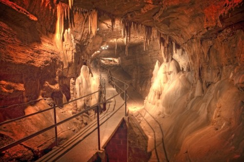 A dimly lit cave with stalactites and stalagmites, featuring a walkway for visitors.