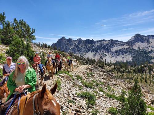 A group of people on horseback riding along a rocky trail with mountains in the background under a clear blue sky.