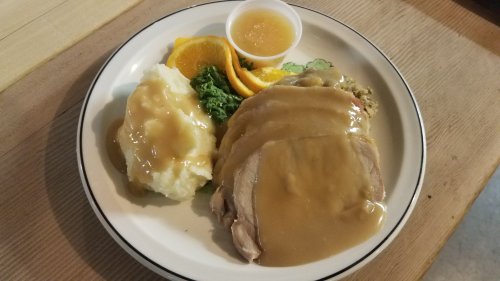 A plate of sliced turkey with gravy, mashed potatoes, greens, orange slices, and a small cup of sauce.