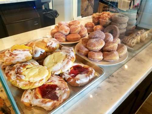 A display case filled with various pastries, including glazed donuts, fruit danishes, and cinnamon rolls.