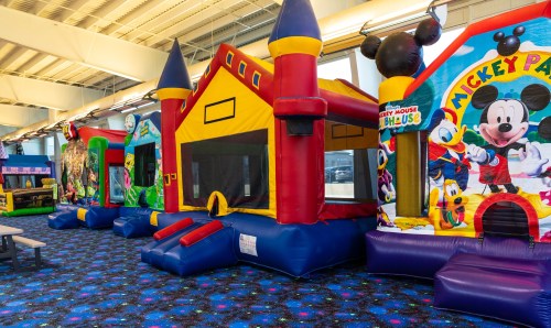 Colorful bounce houses with various themes, including a castle and Mickey Mouse, set in a bright indoor play area.