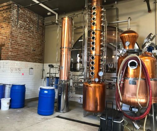 A distillery interior featuring copper stills, barrels, and brick walls, showcasing the distillation process.