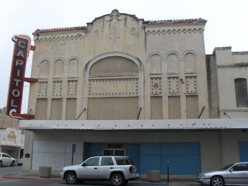 Historic Capitol theater facade with ornate details and a large marquee, featuring a faded sign and parked cars in front.